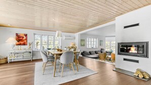 Un'ampia zona giorno con soffitto in legno, un tavolo da pranzo con sedie, un divano, un camino e ampie finestre.