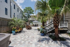 Un patio con piso a cuadros, plantas en macetas, mobiliario exterior y una palmera.