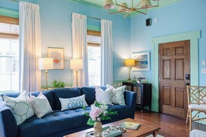 Una sala de estar con un sofá azul, dos lámparas, una puerta de madera y una ventana con cortinas.