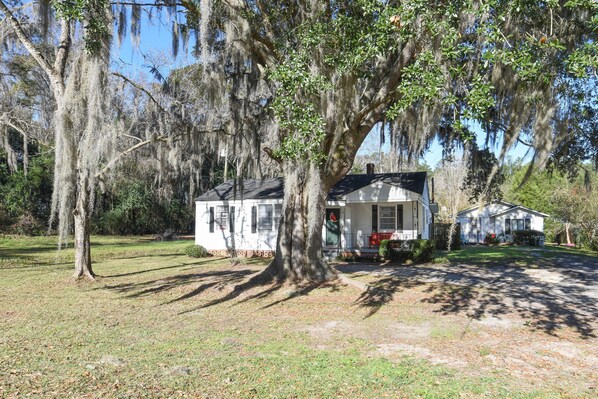Traditional single-story home with a gabled roof and front porch, set amidst a well-manicured lawn and mature trees.