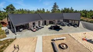 Ein modernes Haus mit überdachter Terrasse, Sitzgelegenheit im Freien und einem Feuerkorb.