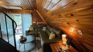 A cozy cabin interior with a wooden interior, a sectional sofa, a small round table, and a window with a view of the outside.