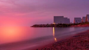 A coastal scene with modern buildings and a calm body of water reflecting the sky.