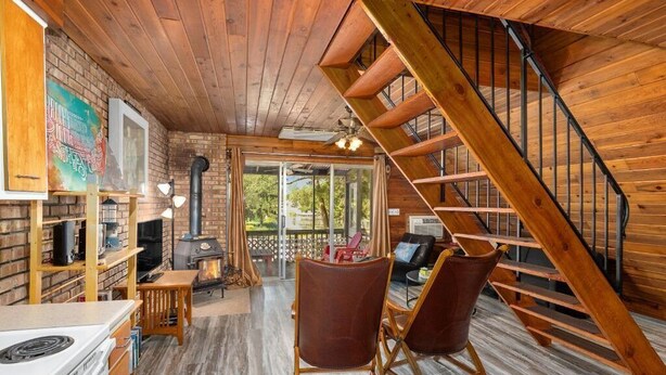 A cozy cabin interior with a wooden staircase, a fireplace, and a dining area.
