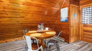 A wooden-paneled room with a round table and chairs, a painting of sailboats, and a checkered curtain.