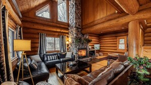 A log cabin interior with a fireplace, leather sofas, and a stone pillar. - THE LUXURY LODGE - SKI, RIDE, GOLF, BIKE, HIKE (Hunter)