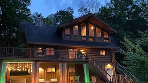 A two-story log cabin with a balcony, large windows, and a porch area with string lights. - THE LUXURY LODGE - SKI, RIDE, GOLF, BIKE, HIKE (Hunter)