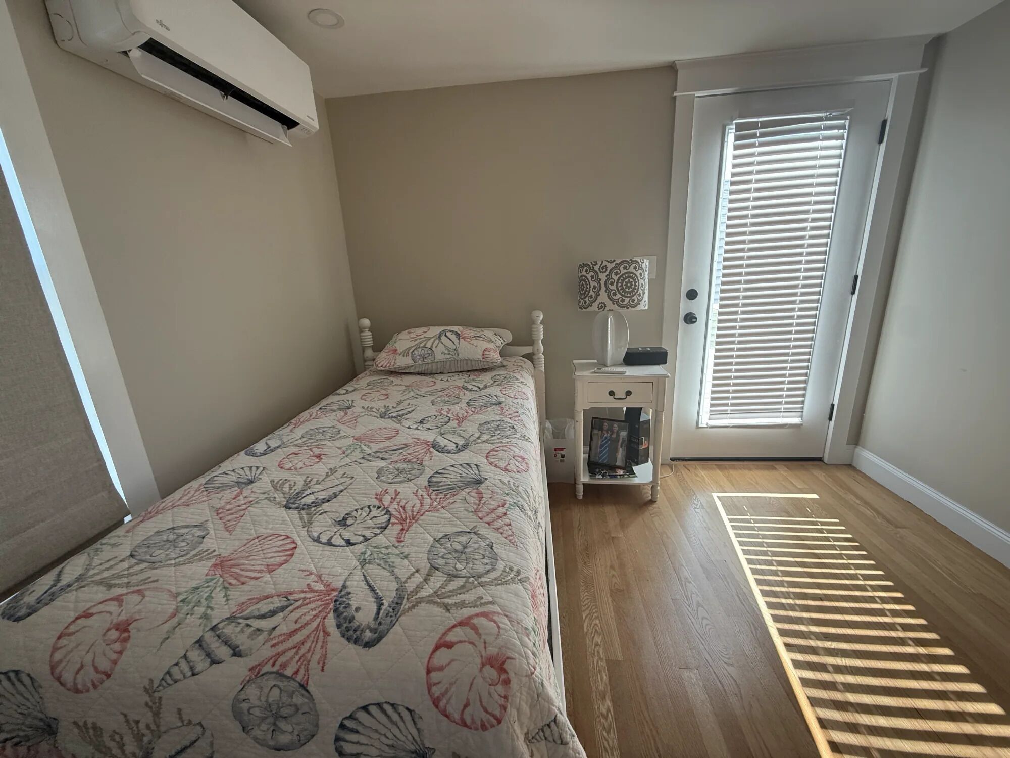 A bedroom with a bed, a nightstand, a lamp, a picture frame, and a door with blinds.