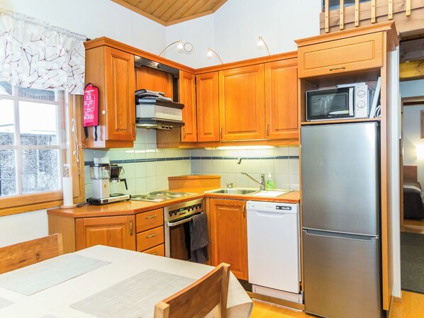 A compact kitchen with wooden cabinets, a stainless steel refrigerator, a dishwasher, and a stove. - Fore camp by Interhome (Nilsiä)