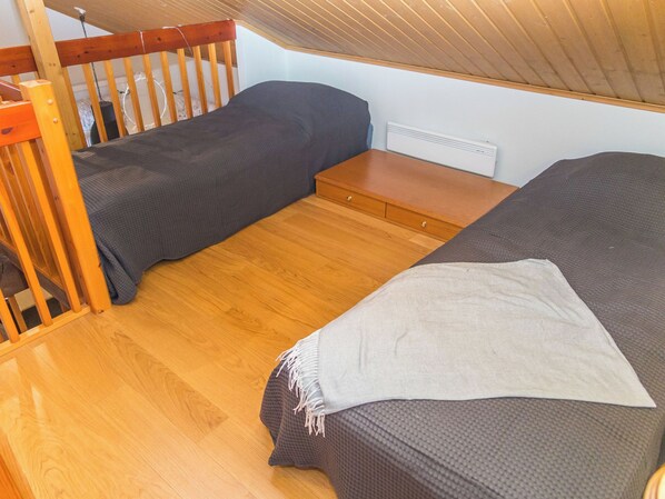 Habitación compacta con dos camas, suelo de madera, una mesita de madera y un radiador blanco.