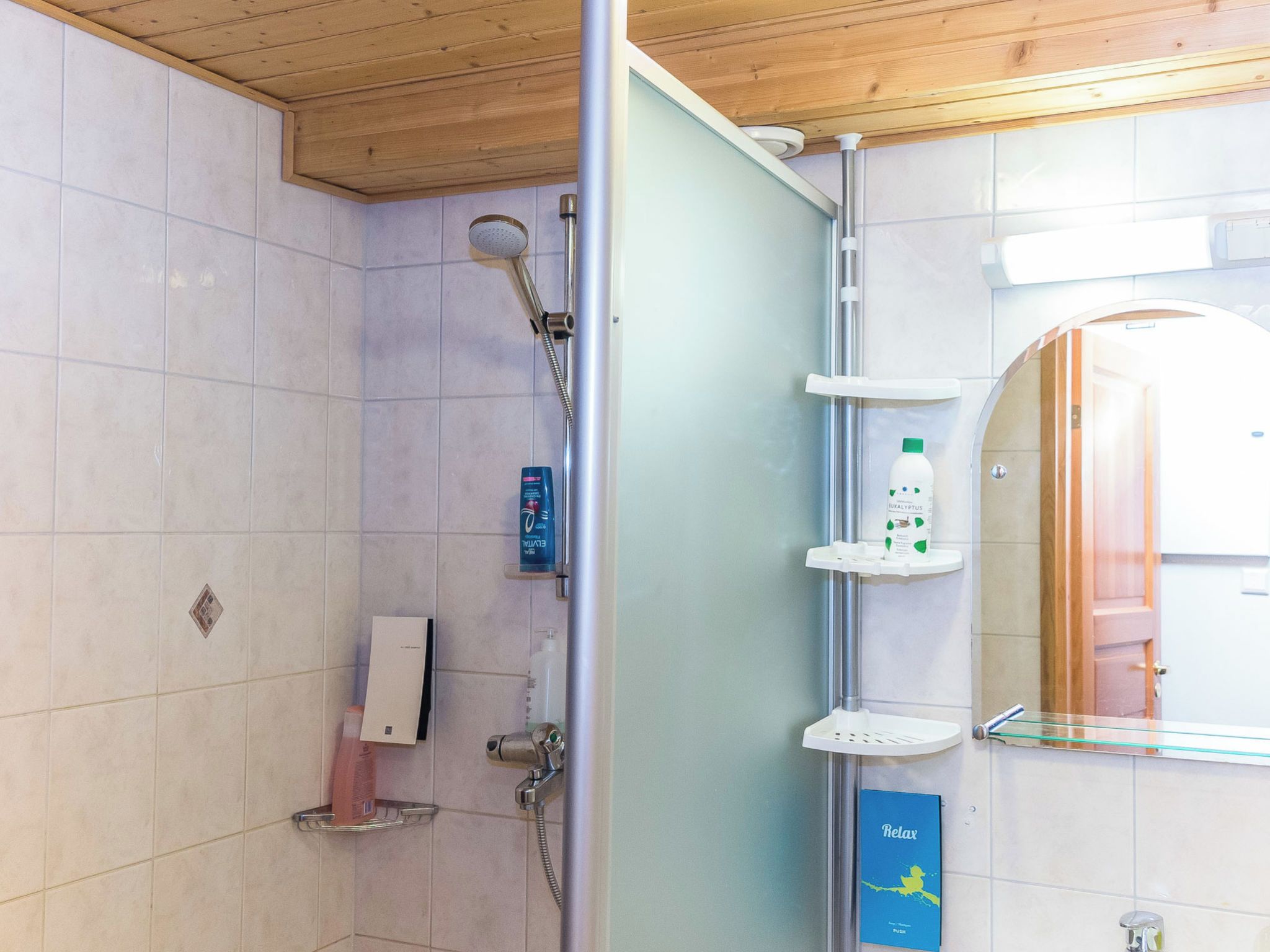 A shower area with a glass partition, a handheld showerhead, a soap dispenser, and a shelf with a bottle.