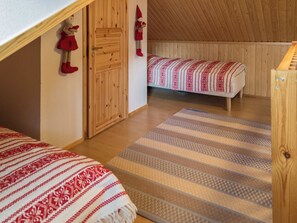 Een knus vertrek met een houten plafond, een bed met een beddeken met een patroon, een houten deur en een klein plankje met decoratieve objecten.