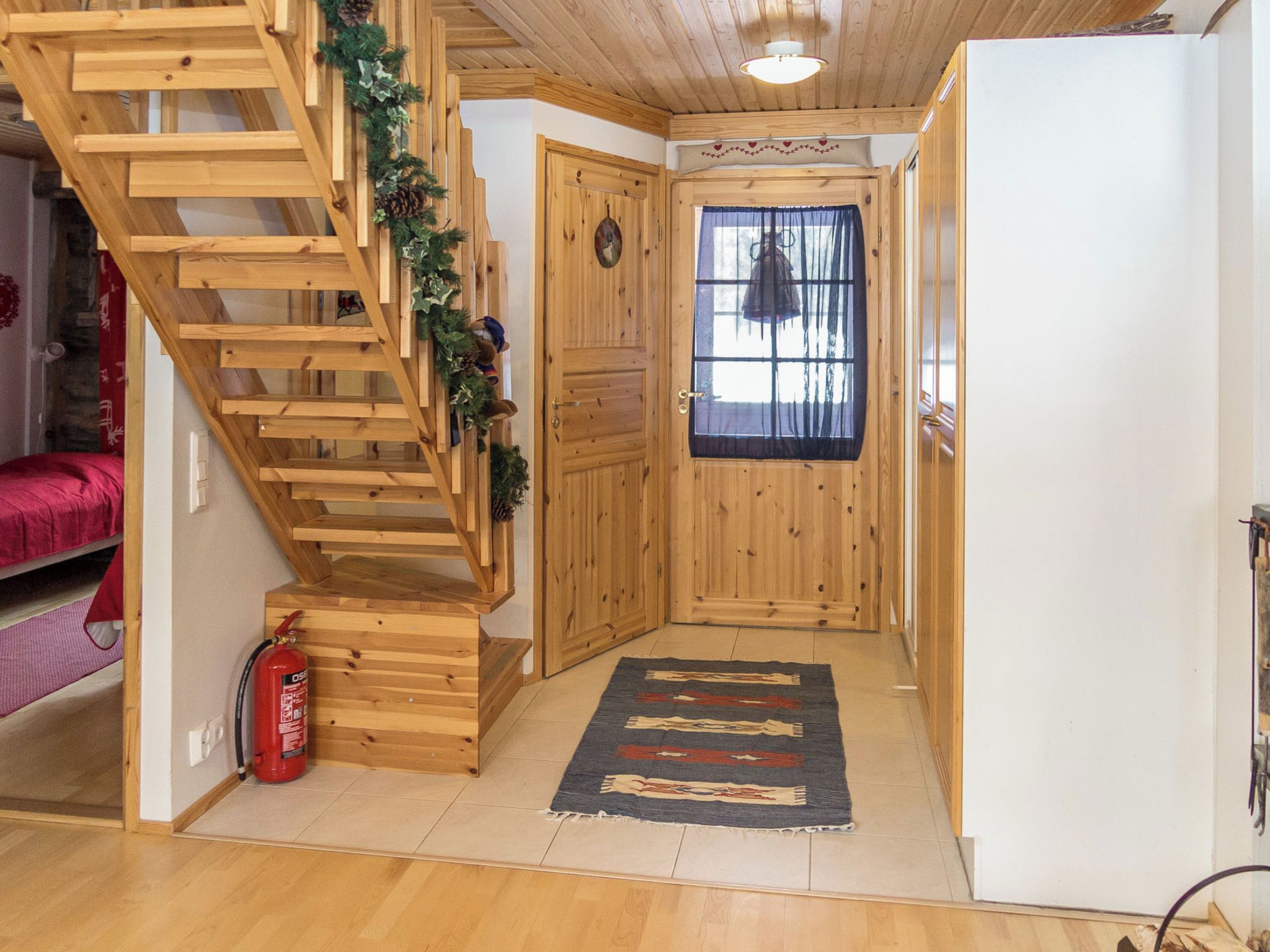 Una escalera de madera con un extintor, una puerta con ventana y un tapete en el suelo.