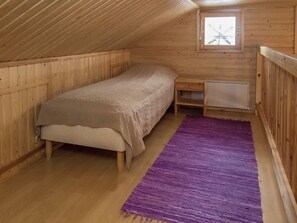 Una cama individual con cabecera, una mesita de noche pequeña, un calentador y una alfombra morada en una habitación de madera con techo inclinado.
