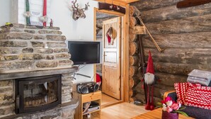 Tunnelmallinen olohuone, jossa on kivinen takka, puuhuonekalut, televisio ja hirsiseinä.