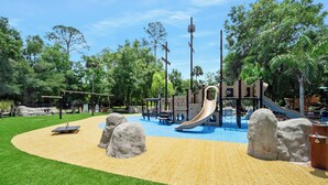 Ein Spielplatz mit Rutschen, Klettergerüsten und einem Sandkasten, umgeben von Bäumen.