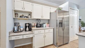 A compact kitchen with white cabinets, a stainless steel refrigerator, a coffee maker, and a blender on the countertop. - Private tropical paradise in the heart of the community! Pool and Welcome Basket (Port Orange)