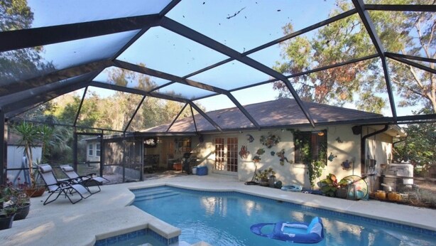 An indoor swimming pool with a glass ceiling, surrounded by lounge chairs and potted plants.