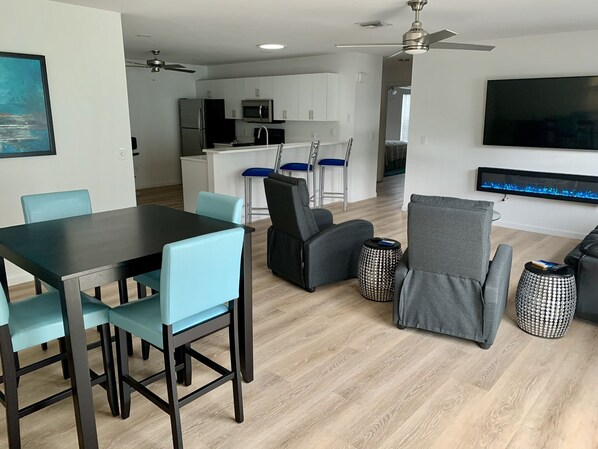 A modern living room with a dining area, kitchen, and a TV mounted on the wall. - Beautifully updated and close to everything!  Yamaha gas cart included! (The Villages)