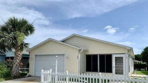 A single-story house with a garage, a white picket fence, and a palm tree in the front yard. - Beautifully updated and close to everything!  Yamaha gas cart included! (The Villages)