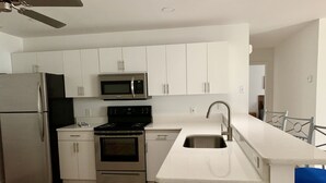 A modern kitchen with white cabinets, stainless steel appliances, and a blue bar stool. - Beautifully updated and close to everything!  Yamaha gas cart included! (The Villages)