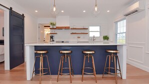 Una cocina moderna con una isla central, taburetes de bar, iluminación colgante y estantes empotrados.