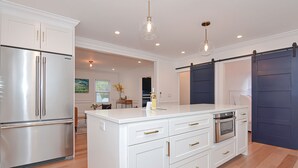 Una cocina moderna con armarios blancos, un refrigerador de acero inoxidable, horno empotrado y una isla grande con detalles dorados.