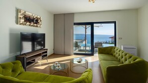 A modern living room with a flat-screen TV, two green sofas, a coffee table, and a view of the sea through a sliding glass door. - Luxurious home in Jesenice with sauna (Jesenice)