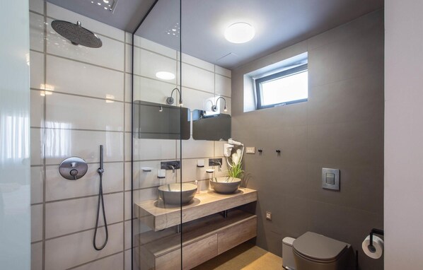 Une salle de bain moderne avec une douche à l’italienne en verre, un meuble-lavabo avec un vasque, un miroir et des toilettes.
