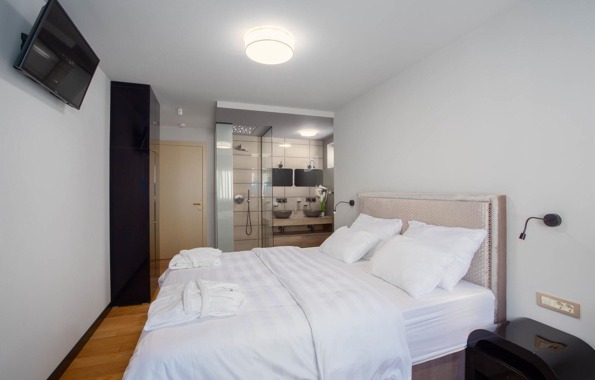A hotel room with a bed, bedside table, and a TV mounted on the wall.