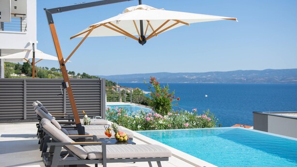 A poolside area with lounge chairs, a table with drinks, and a view of the sea. - Luxurious home in Jesenice with sauna (Jesenice)