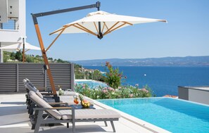 Un espace aménagé au bord de la piscine, avec des chaises longues, une table où sont servis des boissons et une vue sur la mer.
