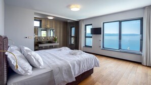 A modern hotel room with a large bed, a bathroom with a vanity, and a large window offering a sea view. - Luxurious home in Jesenice with sauna (Jesenice)