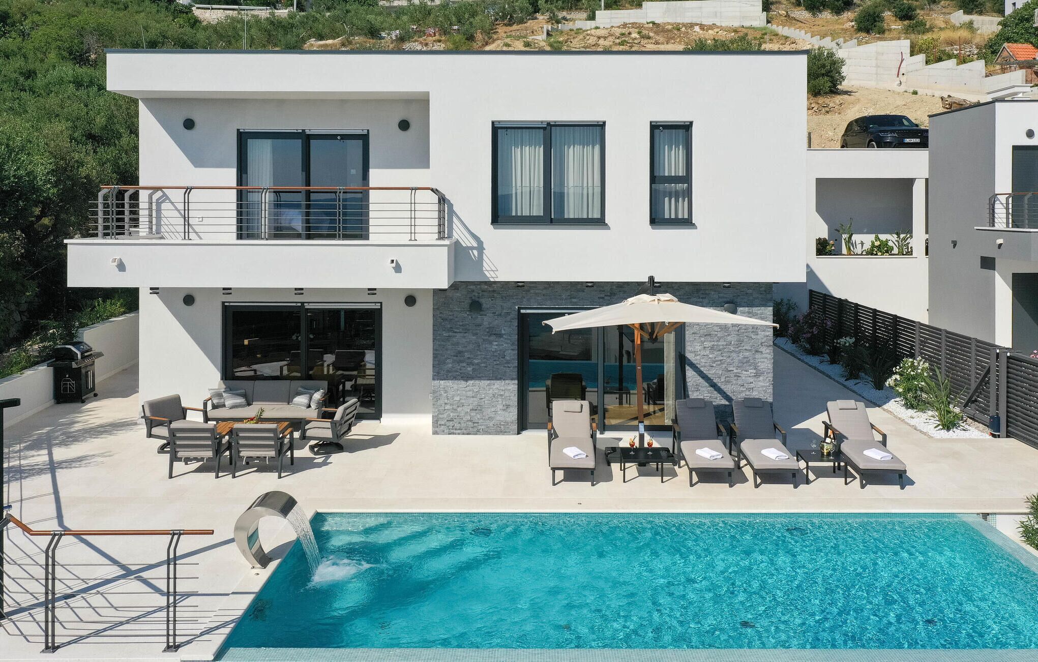A modern two-story house with a swimming pool, outdoor seating, and a balcony.