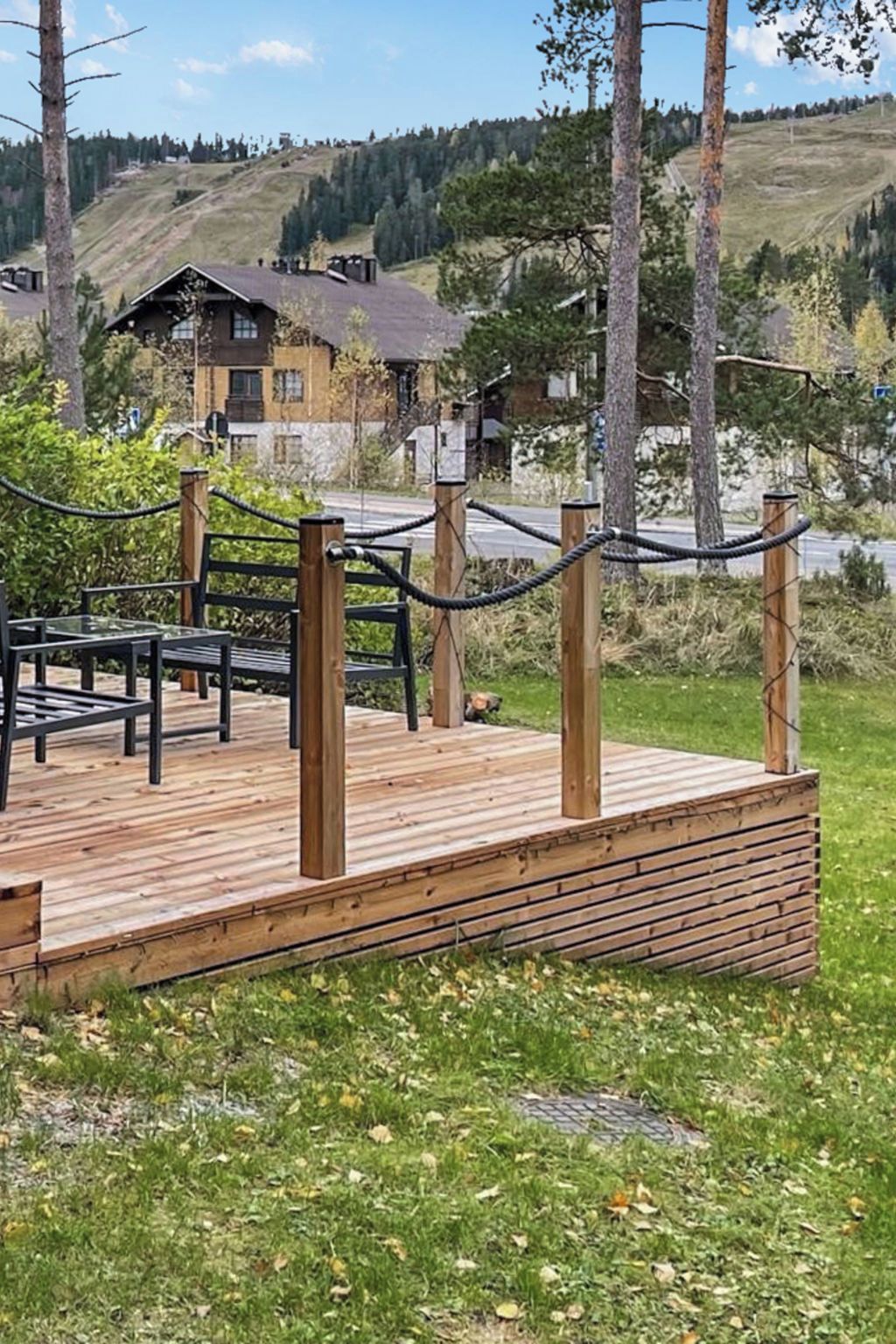 A wooden deck with a table and chairs, surrounded by a rope barrier, overlooking a hilly landscape with buildings in the background.