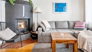 En hyggelig stue med pejs, en grå sofa, en sort lænestol og et træbord.