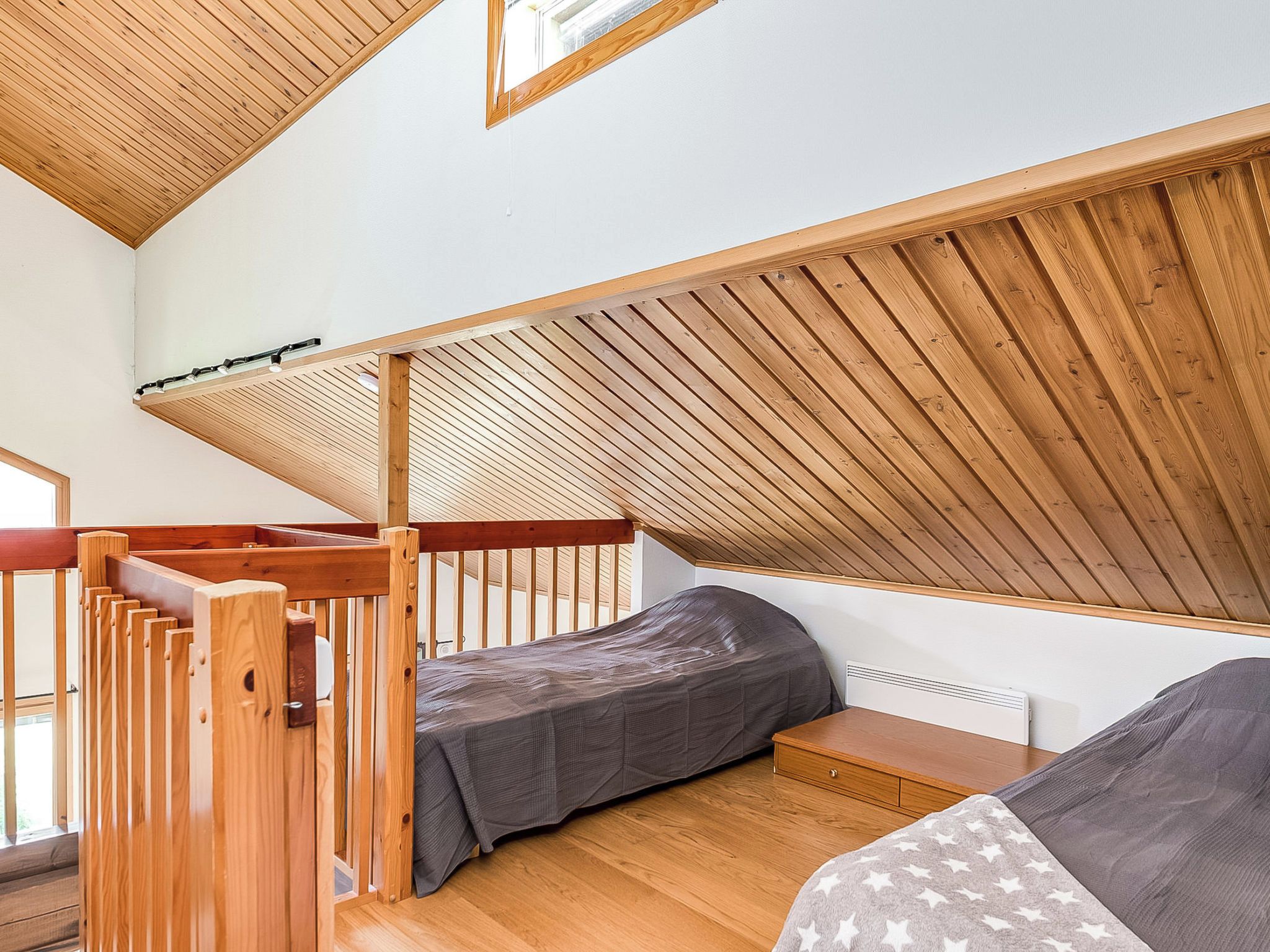 Una habitación pequeña con techo inclinado, cama, un banco y una ventana.
