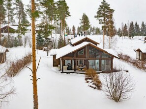 A cabin with a large glass front, surrounded by snow-covered ground and trees.