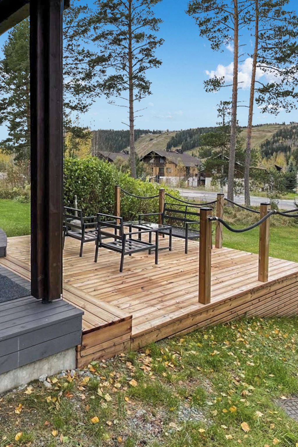 Eine Holzterrasse mit Gartenmöbeln, einem Seilgeländer und Blick auf eine ländliche Landschaft mit Häusern und Bäumen.
