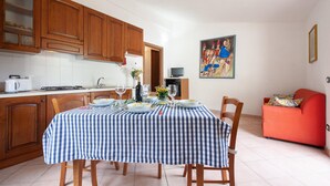 A dining area with a checkered tablecloth, wooden chairs, a red sofa, and a painting on the wall.