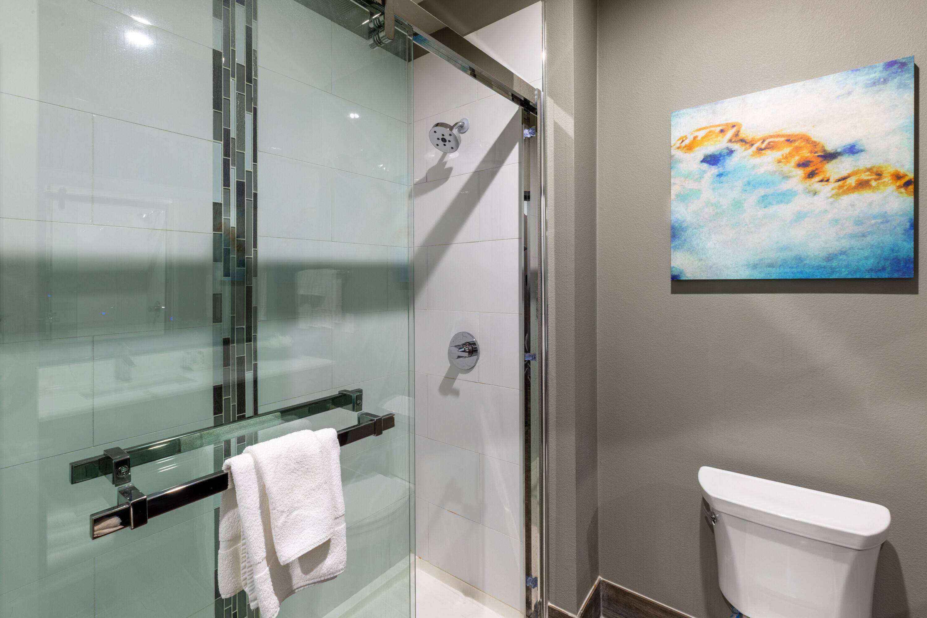 Une salle de bain moderne avec une douche à parois de verre, des toilettes blanches et un porte-serviettes en verre sur lequel est posée une serviette blanche.