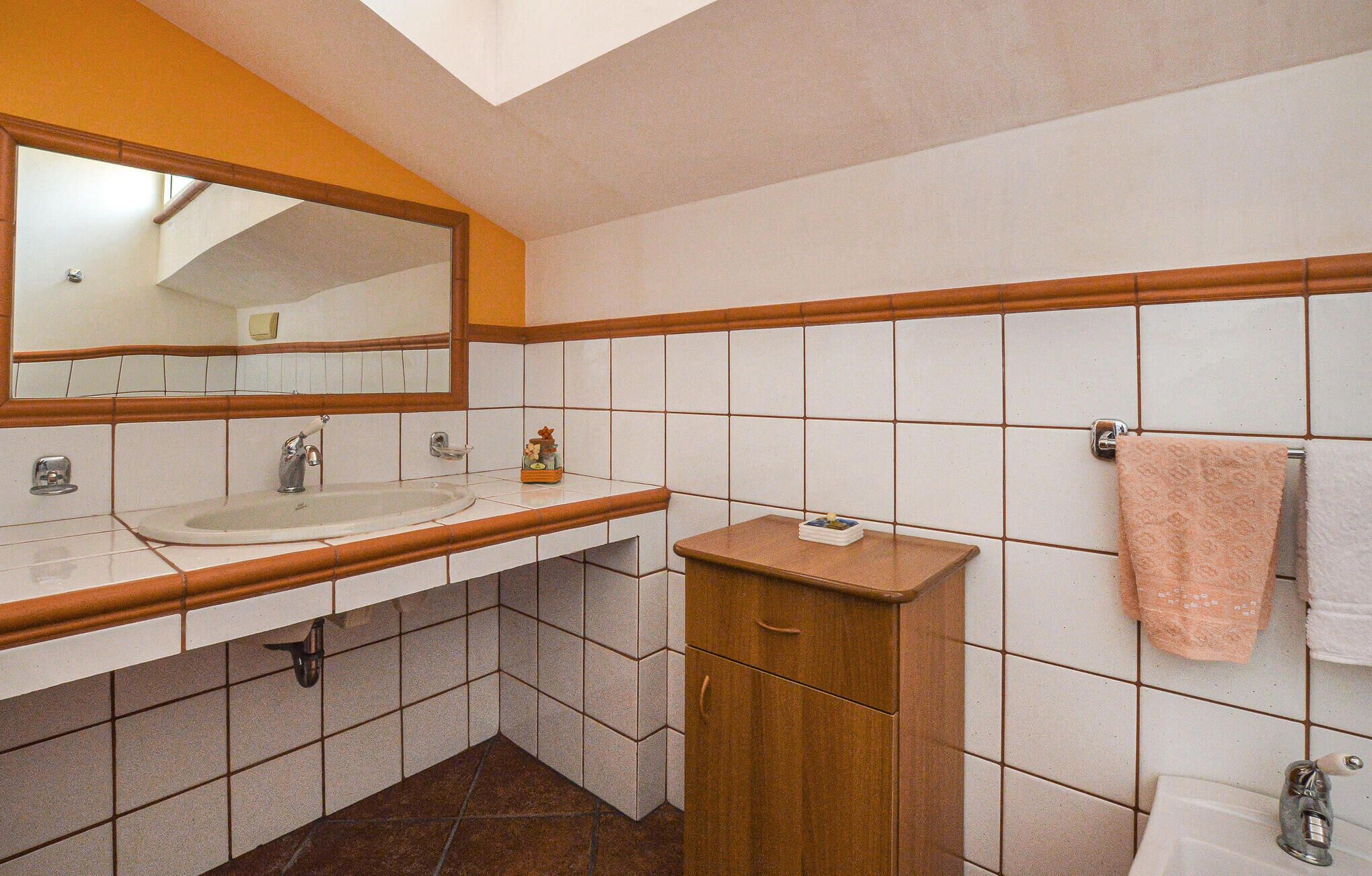 Ein Badezimmer mit weißem Waschbecken, einem Spiegel, einem Holzschrank und einem Handtuchhalter.