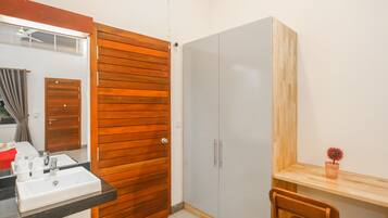 A bathroom with a wooden door, a white sink, a mirror, a wardrobe, and a small wooden table with a potted plant.