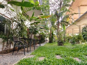 Une cour dotée d’un espace aménagé avec des sièges, entourée de différentes plantes et arbres.