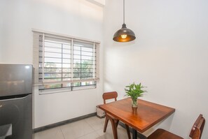 Une cuisine compacte comprenant une table à manger, des chaises, un luminaire suspendu et une fenêtre avec des stores.