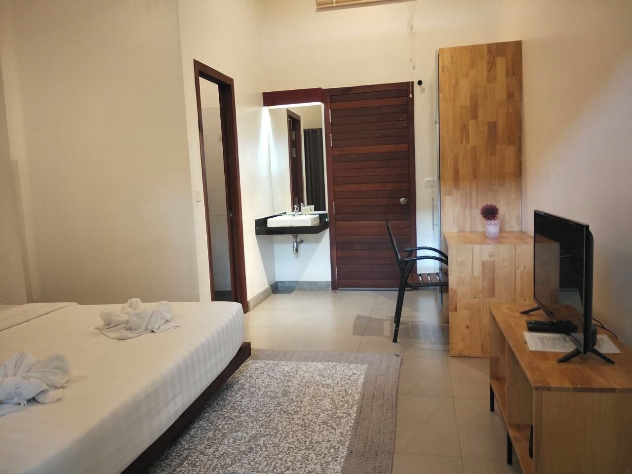 Een hotelkamer met een bed, een bureau met een computer, een houten kledingkast, een badkamer met een wastafel en een spiegel.
