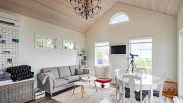 A spacious living room with a large gray sofa, a white round table, and a white chair. There is a chandelier, a telescope, and a birdcage on the right side.