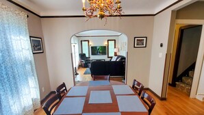 Ein Esszimmer mit Holztisch, Stühlen, einer Chandelierleuchtre und Blick ins Wohnzimmer.