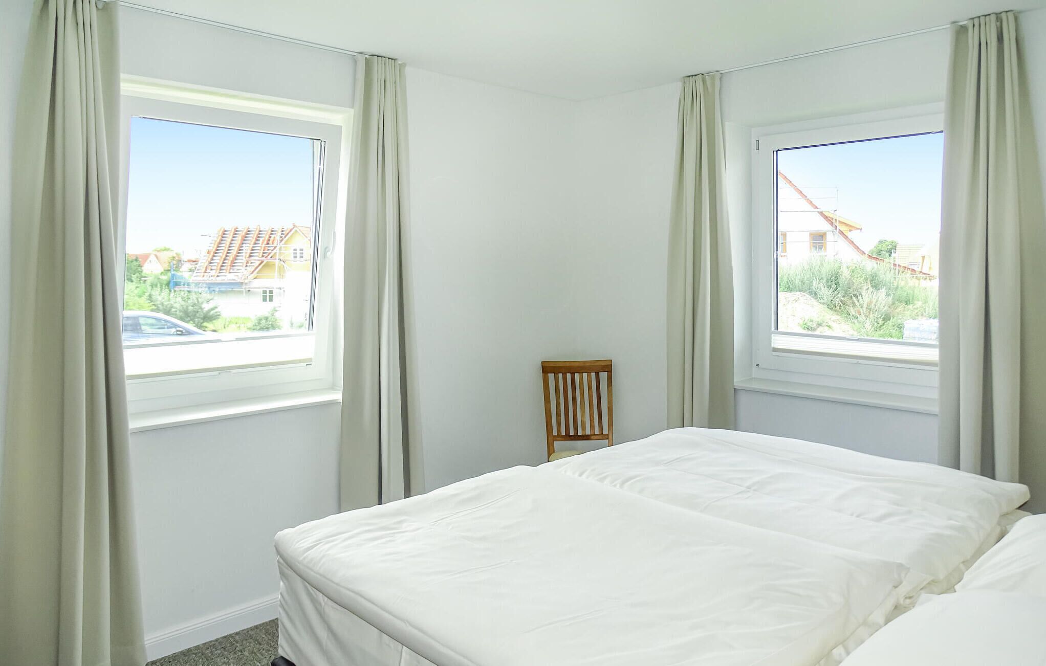 A bedroom with a bed, two windows, and a chair.
