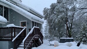 A snow-covered house with a wooden deck and steps leading to the front door. - Vista Chalet-Yosemite and Bass Lake getaway with Tesla charger (Oakhurst)